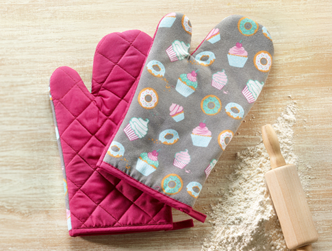 Bunte Ofenhandschuhe mit Cupcake-Muster auf Holzuntergrund und Mehl