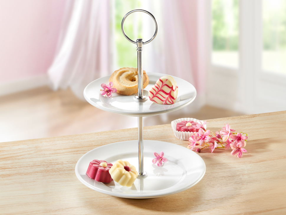 Zweistufige Etagere mit Gebäck auf Holztisch vor hellem Fenster.