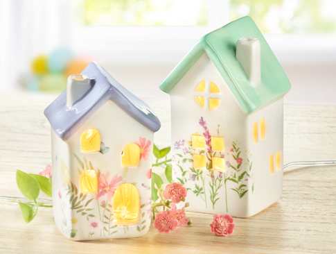 Zwei leuchtende Keramikhäuschen mit Blumenmotiv auf Holztisch