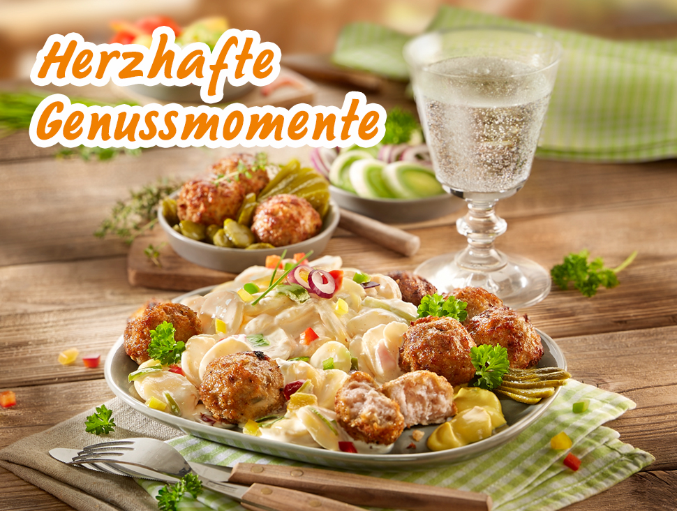 Klopse mit cremigem Kartoffelsalat, Gurken und Petersilie auf gedecktem Tisch