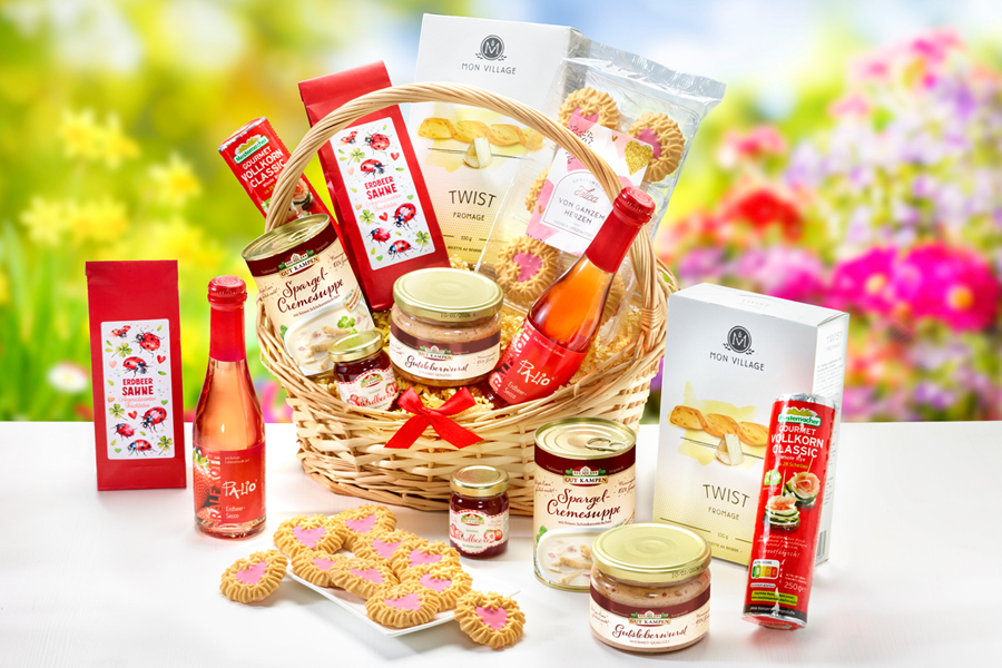 Geschenkkorb mit süßen und herzhaften Leckereien vor blumigem Frühlingshintergrund