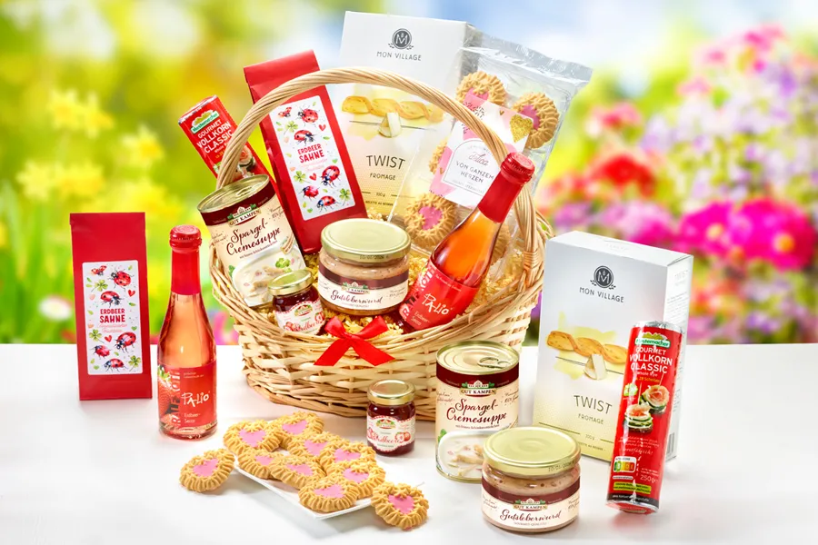 Geschenkkorb mit süßen und herzhaften Leckereien vor blumigem Frühlingshintergrund