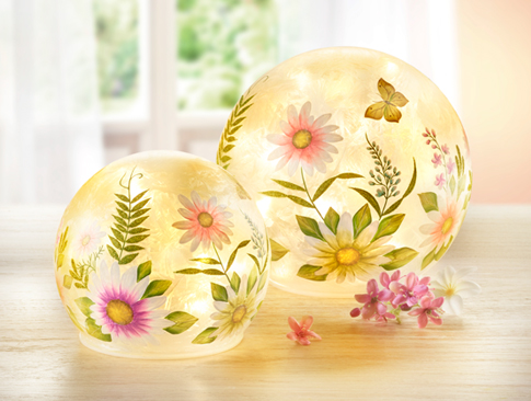Zwei leuchtende Dekokugeln mit Blumenmotiv auf Holztisch.