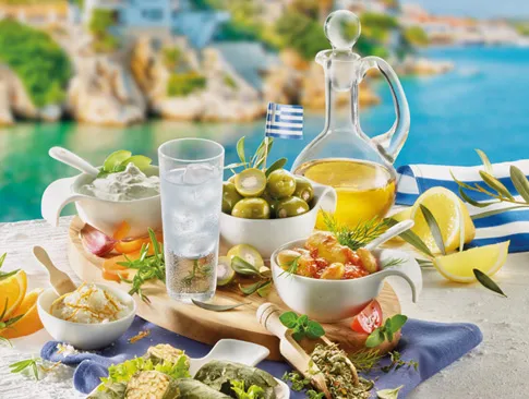 Griechische Spezialitäten mit Oliven, Feta, Öl und Ouzo vor mediterraner Kulisse