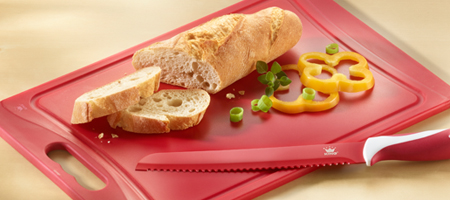 Rotes Schneidbrett mit Brotmesser, Baguette und Gemüse