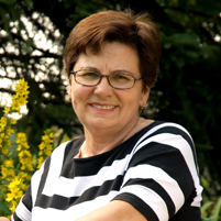 Lächelnde Dame mit Brille in gestreiftem Shirt vor grünem Hintergrund.