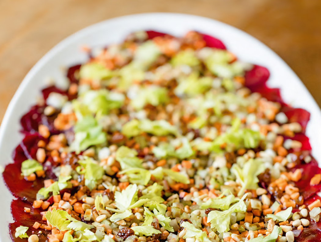 Rote-Bete-Carpaccio mit Nüssen, Salat und Dressing auf einem weißen Teller.