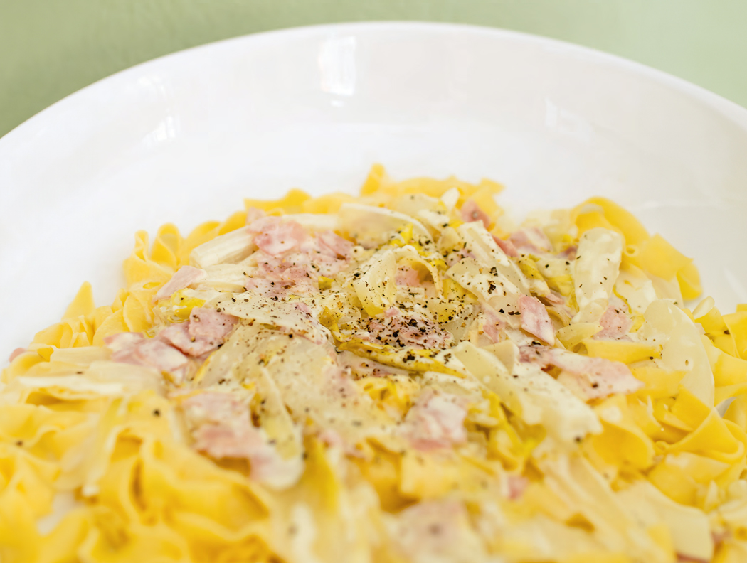 Tagliatelle mit Sahnesoße, Schinken und Käse auf einem weißen Teller.