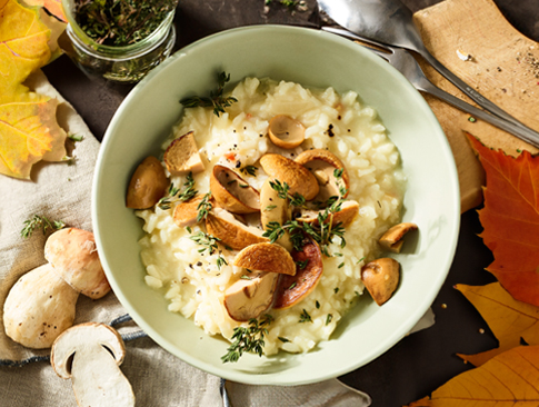 Cremiges Pilzrisotto mit frischen Kräutern und Waldpilzen in herbstlicher Deko
