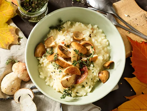 Cremiges Pilzrisotto mit frischen Kräutern und Waldpilzen in herbstlicher Deko
