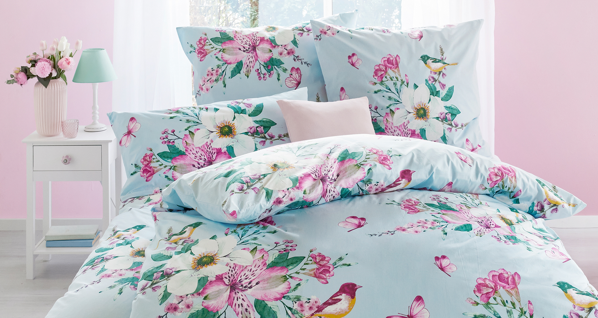 Bettwäsche mit Blumen- und Vogelmotiv in hellem Schlafzimmer.