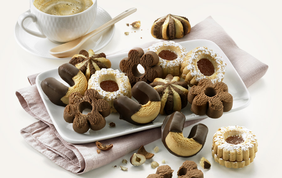 Feines Gebäck mit Schokolade und Nüssen auf Teller, dazu eine Tasse Kaffee.