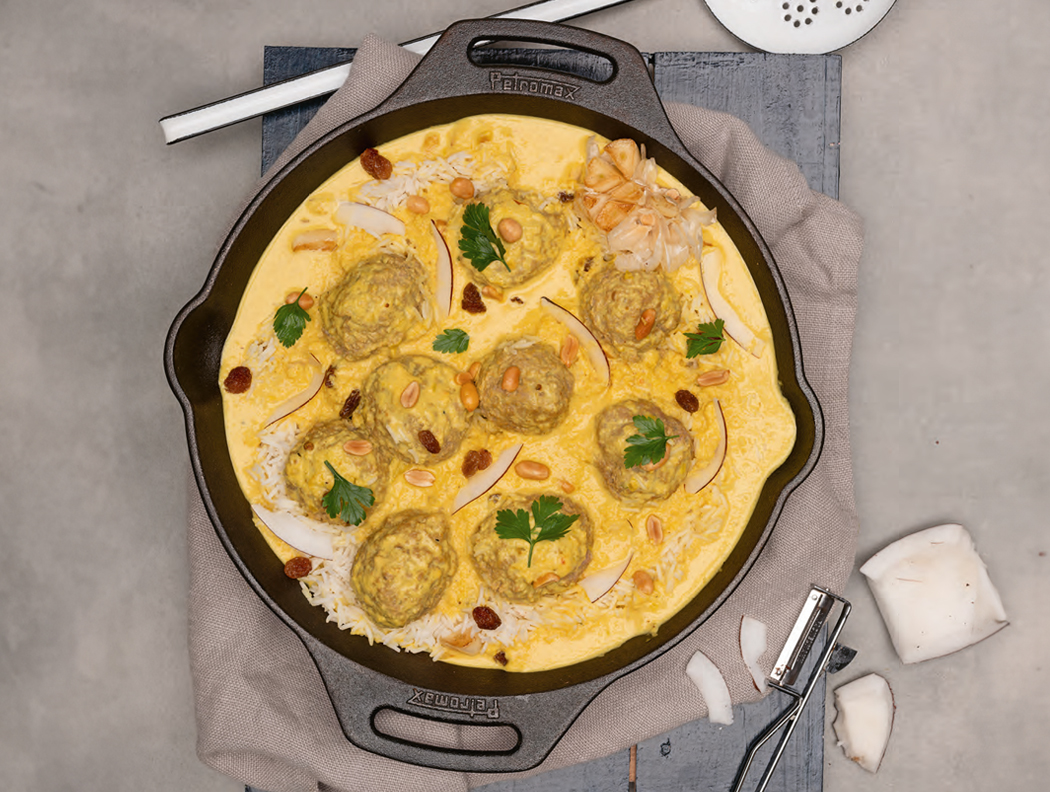 Fleischbällchen in cremiger Currysauce, garniert mit Kräutern in einer Pfanne.