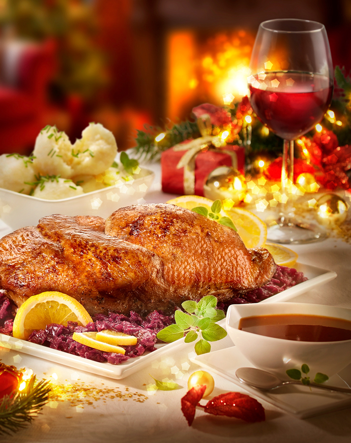 Festlicher Braten mit Rotkohl, Klößen und Wein auf weihnachtlich gedecktem Tisch