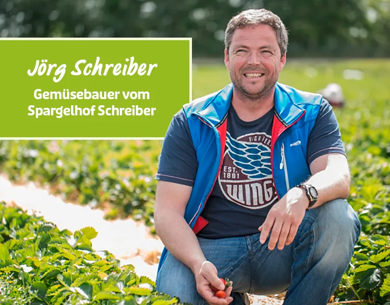 Gemüsebauer sitzt auf dem Feld und lächelt in die Kamera