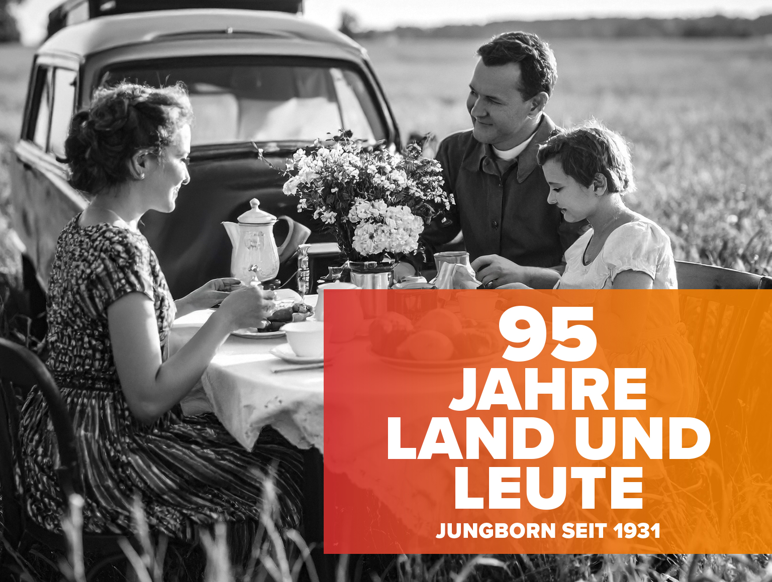 Historische Szene mit Familie beim Essen im Freien, Schriftzug „95 Jahre Land und Leute“