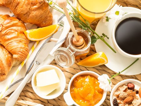 Frühstück mit Croissants, Honig, Marmelade, Kaffee und Orangensaft.