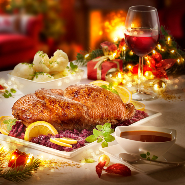 Festlicher Braten mit Rotkohl, Klößen und Wein auf weihnachtlich gedecktem Tisch