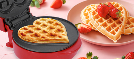 Rotes Waffeleisen mit Herzwaffel und angerichteten Waffeln mit Erdbeeren