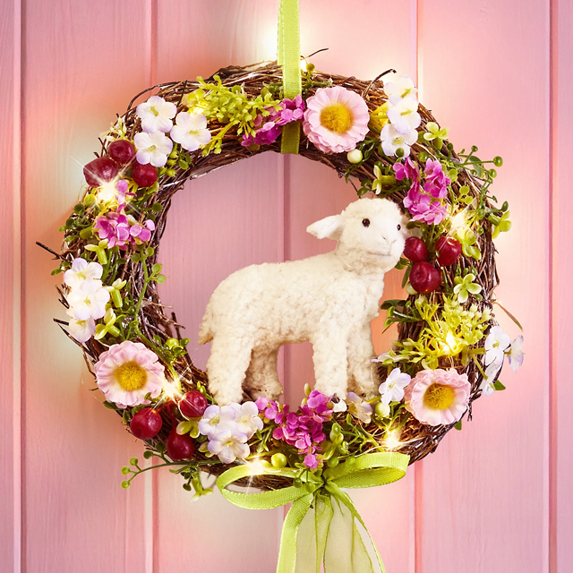 Blumenkranz mit Lammfigur vor rosa Hintergrund, Text ›Zauberhafte Ostervorboten