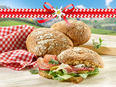 Südtiroler Bauernbrot mit Schinken, Salat und Käse auf Holztisch vor Alpenkulisse