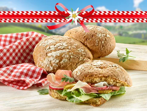 Südtiroler Bauernbrot mit Schinken, Salat und Käse auf Holztisch vor Alpenkulisse