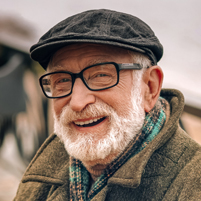 Lächelnder älterer Mann mit Brille, Mütze und Schal im Outdoor-Bereich.