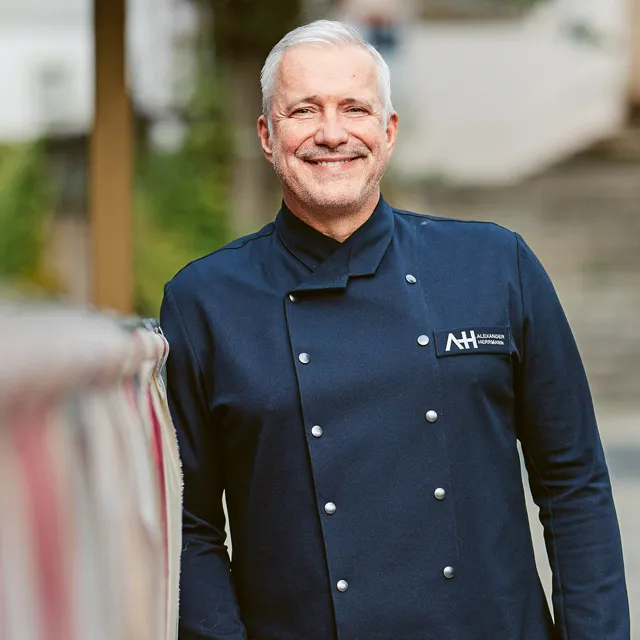 Alexander Herrmann lächelt in dunkelblauer Kochjacke