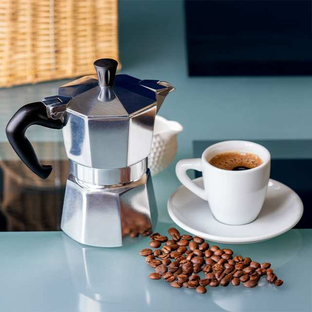 Espressokocher mit Tasse und Kaffeebohnen auf Tisch