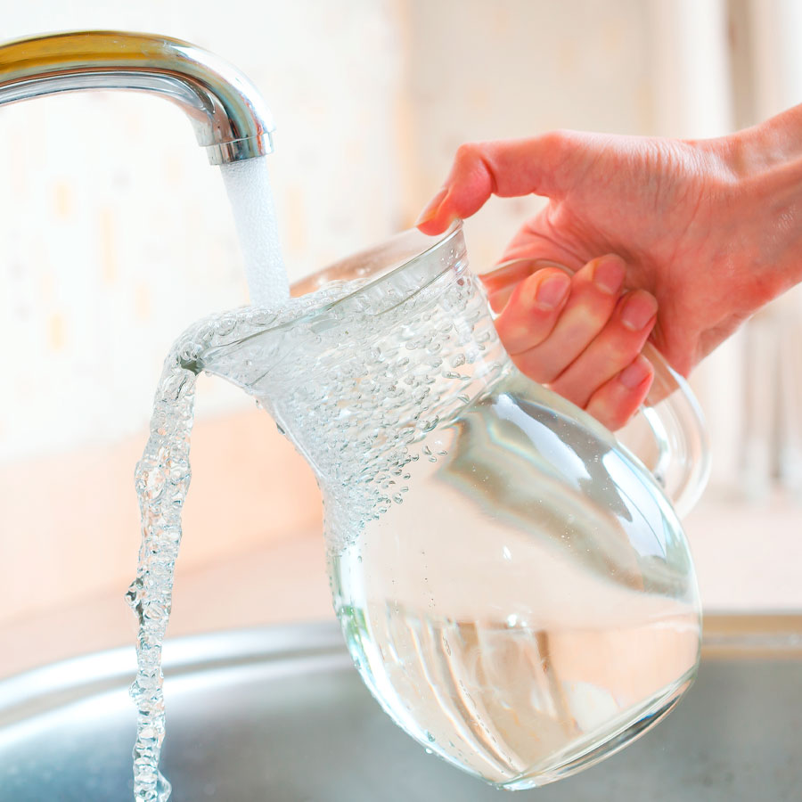 Krug wird unter fließendem Wasserhahn mit Wasser gefüllt