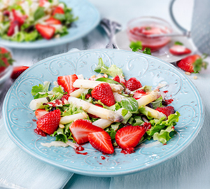 Frischer Spargelsalat mit Erdbeeren und grünem Salat auf einem blauen Teller