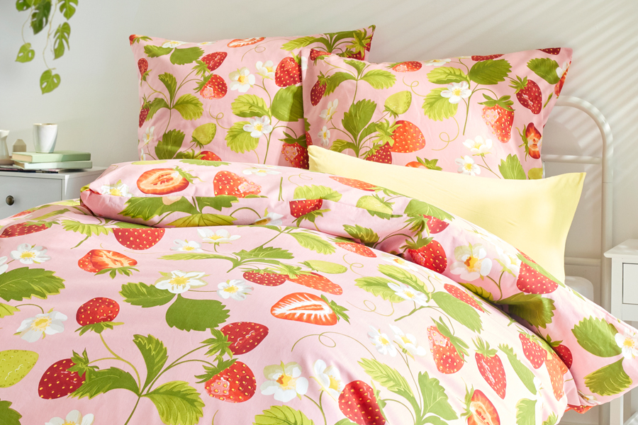 Bettwäsche mit Erdbeermotiv in Rosa-Grün auf einem weißem Metallbett
