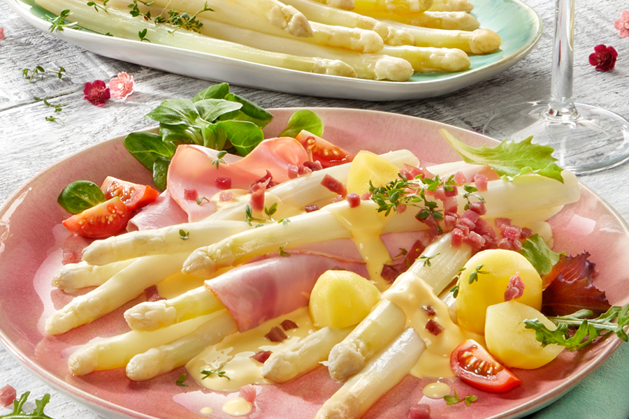 Weißer Spargel mit Schinken, Kartoffeln und Sauce Hollandaise auf rosa Teller
